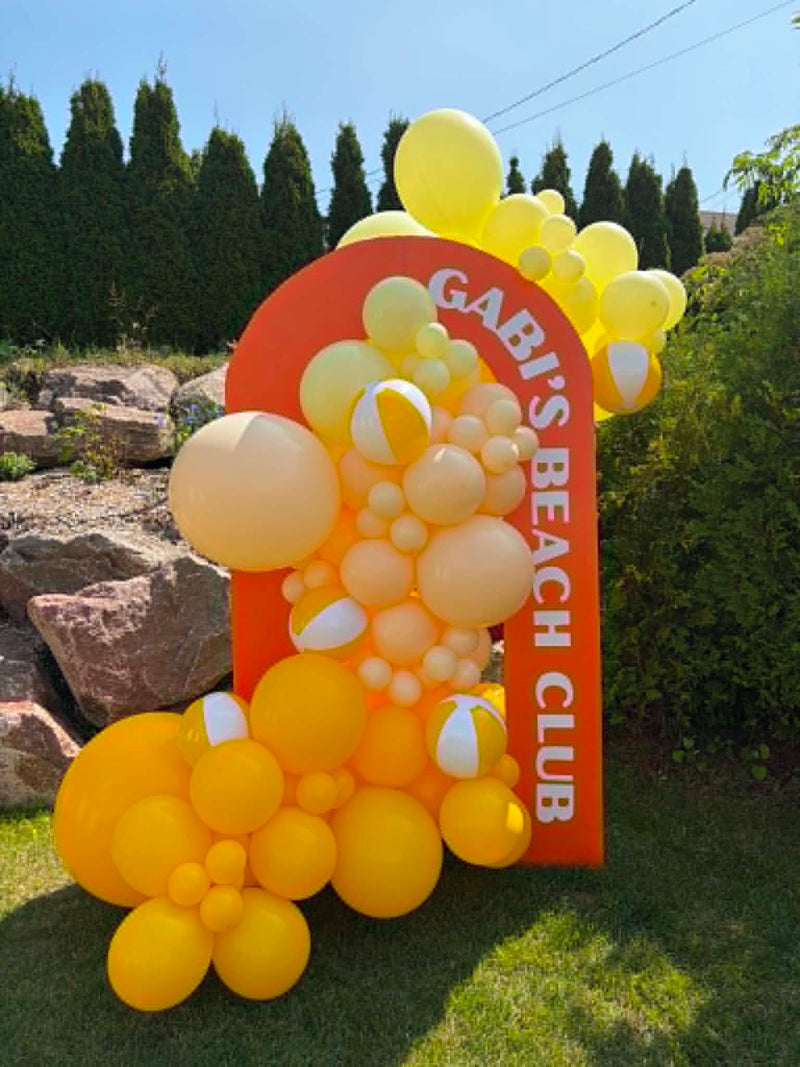 Ballons jaune et crème autours d'une arche orange ave l'inscription Gabi's Beach Club