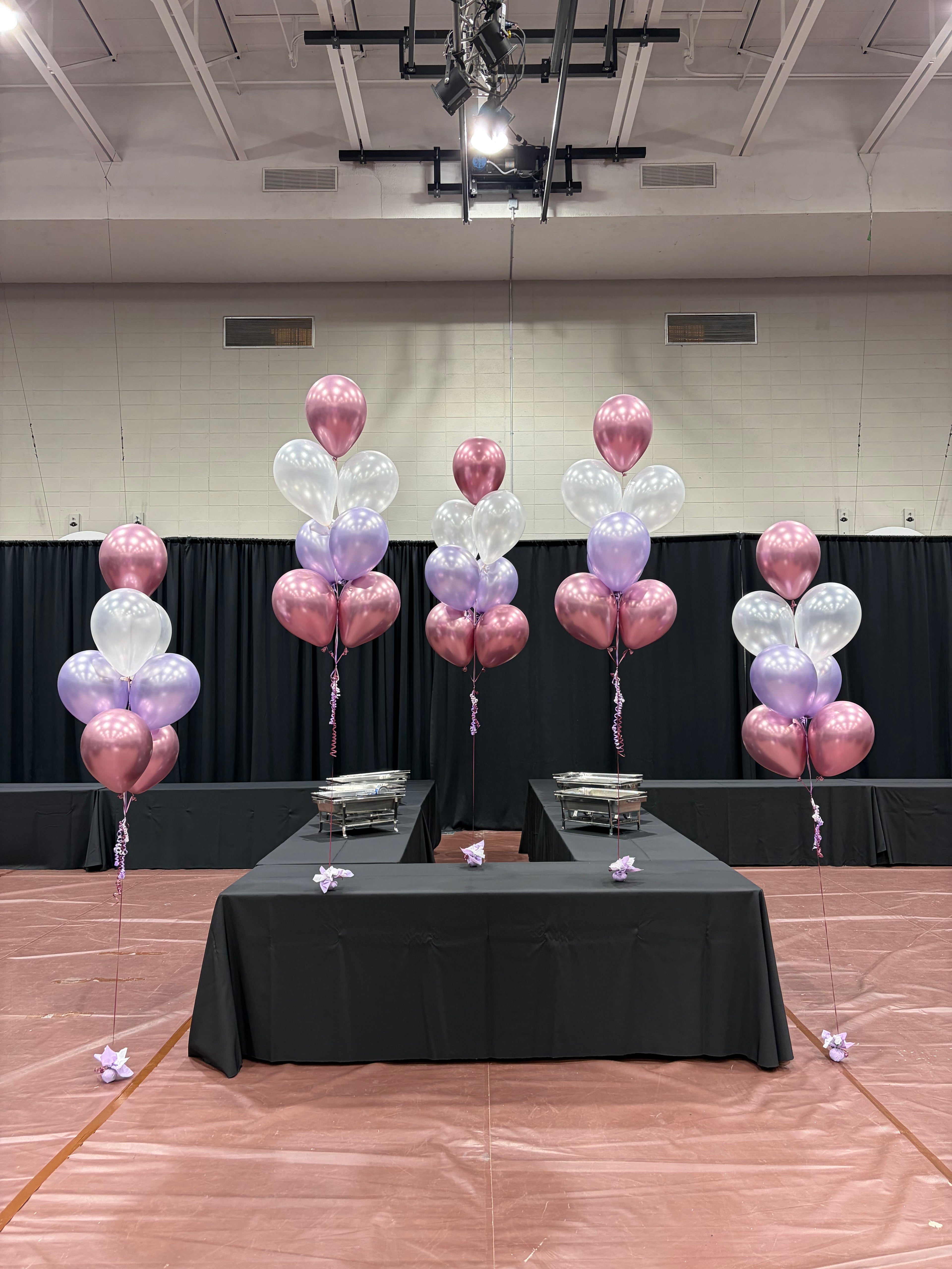 Cinq bouquets de ballons aux couleurs rose, mauve et blanc sur une table de banquet pour un évènement de graduation à Québec